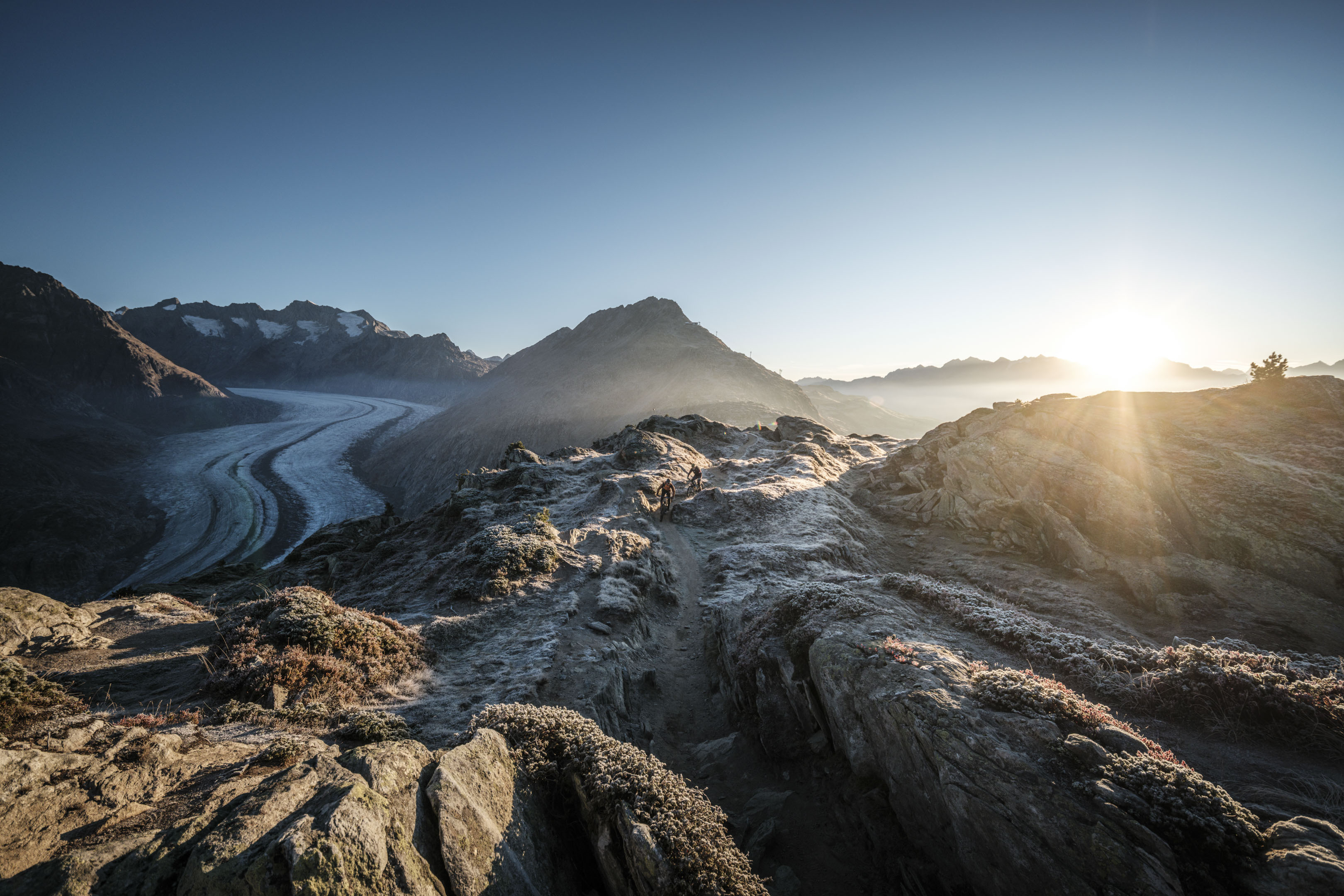 Frühlingsfahrten Hohfluh mit einem Paar in bunten Jacken auf einer Bank mit Blick auf den Grossen AletschgletscherSpring rides Hohfluh with a couple in colorful jackets on a bench with a view of the Great Aletsch GlacierCourses printanières à Hohfluh avec un couple en vestes colorées sur un banc avec vue sur le grand glacier d'Aletsch